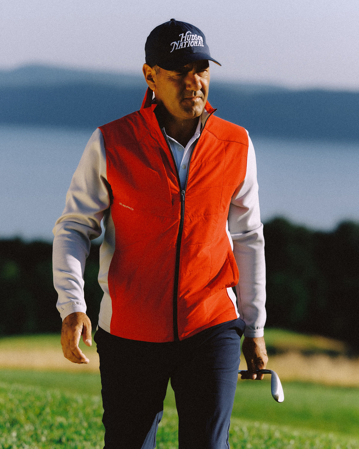 Woman walking the course in a tan jacket, holding a club