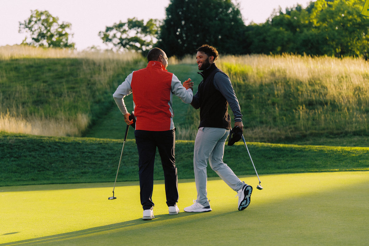 Two golfers carrying bags across the fairway